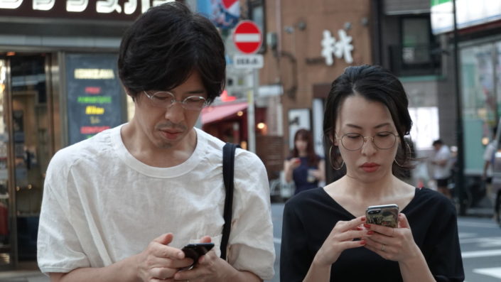 Mies ja nainen katsovat kännyköitään kadulla Tokiossa.