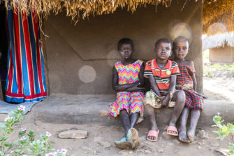 Kolme ugandalaista lasta istuu talon edessä.