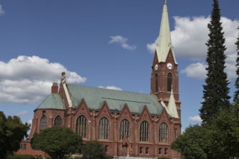 Punatiilinen kirkkorakennus taustalla sininen taivas ja pilviä