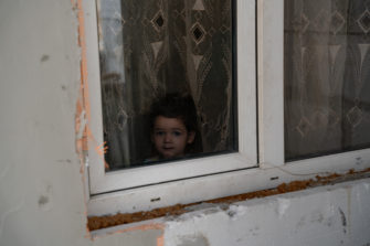 Pieni tyttö kurkkaa rikkinäisestä Ikkunasta Ukrainassa