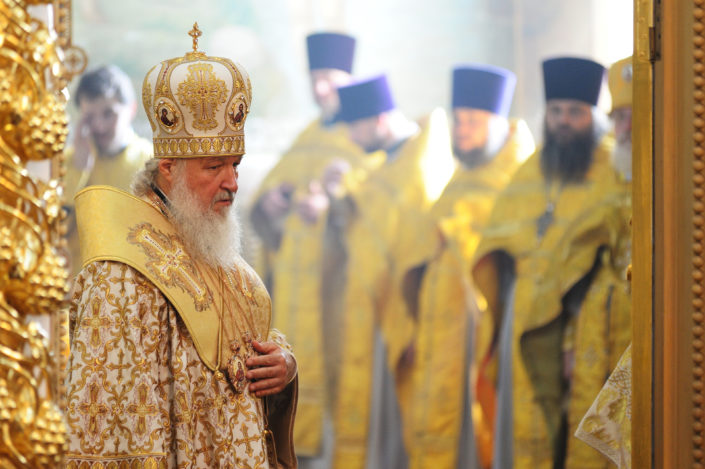 Venäjän-ortodoksikirkon-patriarkka-virallisessa-asussaan-sivuttain-taustalla-kirkollisiin-asuihin-pukeutuneita-miehiä