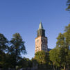 kivinen-kirkon-torni-taustalla-lehtipuita-kuvassa-etualalla