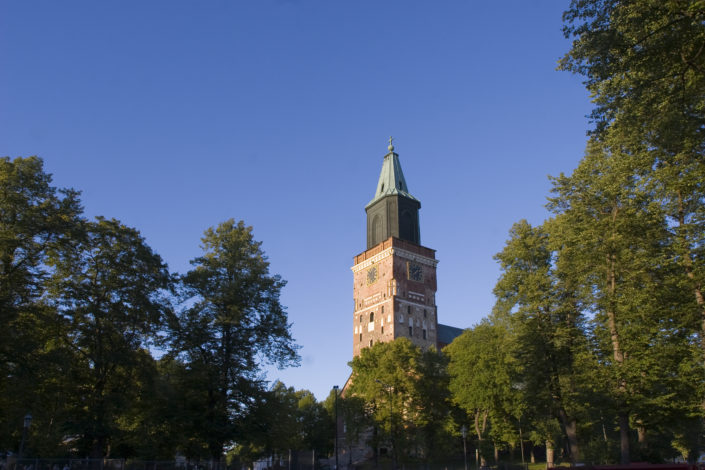 kivinen-kirkon-torni-taustalla-lehtipuita-kuvassa-etualalla