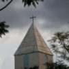 Pilvistä taivasta vasten piirtyy kirkon torni, jonka huipulla on risti.