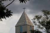 Pilvistä taivasta vasten piirtyy kirkon torni, jonka huipulla on risti.