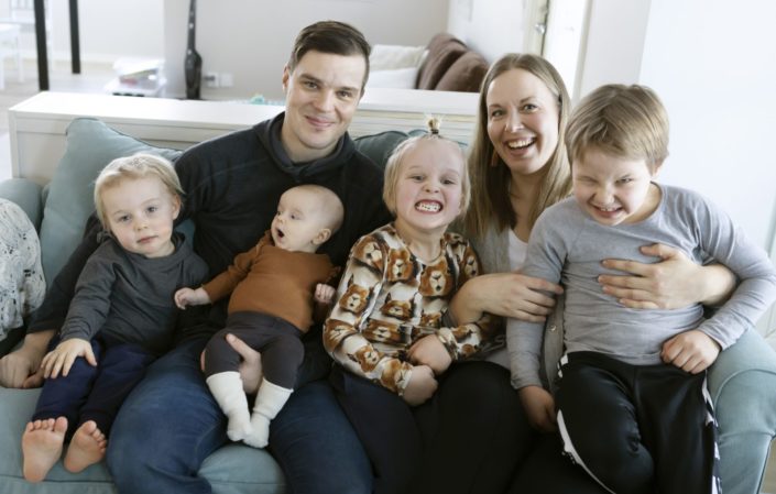 isä, äiti ja neljä pientä lasta iloisina sohvalla