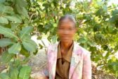 Laosilainen nainen siisteissä vaatteissaan puiden lehvästön ympäröimänä. Hänen kasvonsa ovat sumennetut.