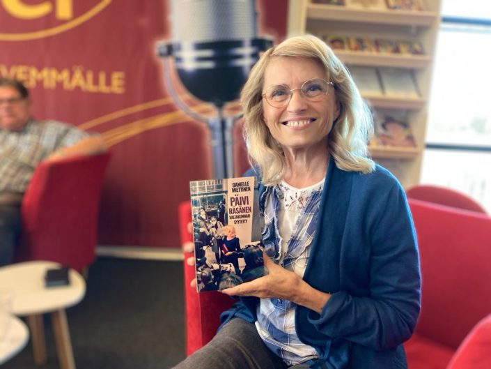 Päivi Räsänen hymyilee Radio Dein studiossa sylissään kirja Päivi Räsänen - Valtakunnansyytetty