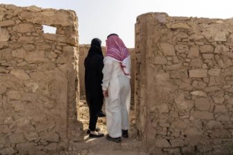 Mustaan huntuun verhottu nainen ja saudimies seisovat kirkon raunioissa.