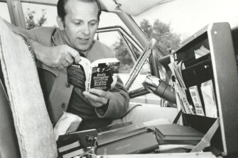 mustavalokuva, jossa mies on autossa ja lukee kirjaa