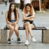 kaksi nuorta pitkähiuksista tyttöä istuu penkillä