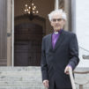 harmaa-hiuksinen-vanha-mies-seisoo-kirkon-portailla-päällään-hänellä-on-piispan-paita