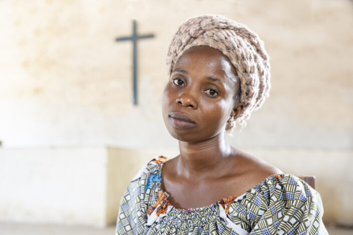 Kongolainen nainen kuviollisessa asussa. Taustalla näkyy risti.