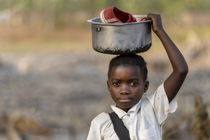 Kongolainen lapsi pitää astiaa päänsä päällä. Astiassa on kengät.
