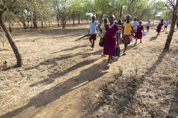 Stella ja Samson ja joukko muita lapsia kävelemässä kouluun hiekkatietä pitkin.