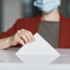 Maskia pitävä nainen pudottamassa äänestyslipuketta laatikkoon.