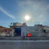 Vaatimaton matala tehdasrakennus ja aurinko paistamassa sen takaa