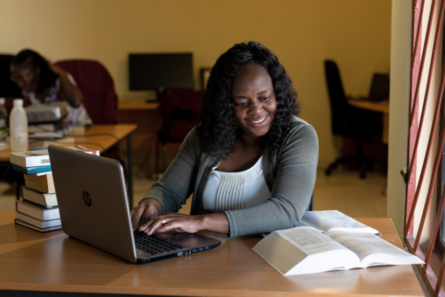 nainen istuu pöydän ääressä, edessä kannettava tietokone ja Raamattu