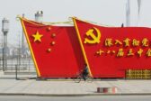 Kaksi suurta punaista lipun mallista seinämää kadulla, molemmat Kiinan lipun tyylisiä. Lipuissa lukee kiinaksi propagandalauseita.