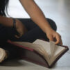 Lapsi lukee sisätiloissa lattialla violettikantista Raamattua risti-istunnassa. Kuvassa näkyy vain osa käsistä ja jaloista.