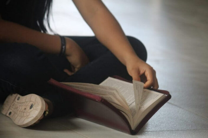 Lapsi lukee sisätiloissa lattialla violettikantista Raamattua risti-istunnassa. Kuvassa näkyy vain osa käsistä ja jaloista.