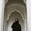 Mustaan hunnutettu nainen vaalean moskeijan pylväikössä.