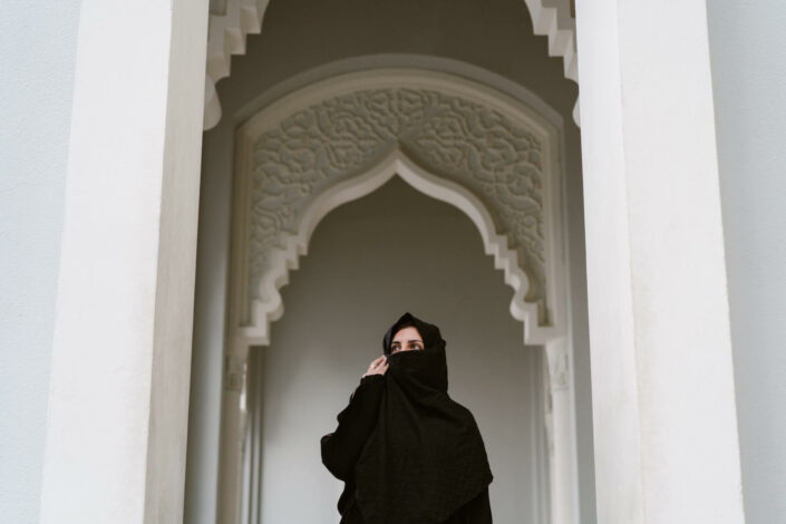 Mustaan hunnutettu nainen vaalean moskeijan pylväikössä.