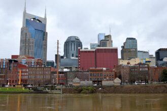 Kuvassa on Nashvillen kaupungin silhuetti. Kaupungissa on sekä korkeita että matalampia rakennuksia. Osa rakennuksista on hyvin moderneja ja lasipintaisia, osa taas vanhempia tiilirakennuksia.