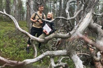 mies ja nainen seisovat metsässä. Etualalla kelottunut puunrunko.