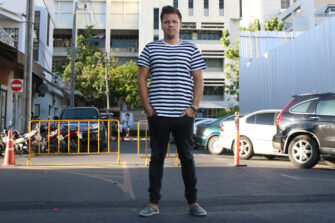 Mies seisoo parkkipaikalla mustavalkoraidallisessa t-paidassa ja mustissa farkuissa.