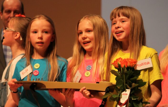 Kolme lasta laulamassa virsikirjat kädessä
