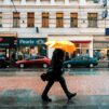 Mies kävelee rivakasti sateenvarjon alla sateisella kaupungin kadulla.