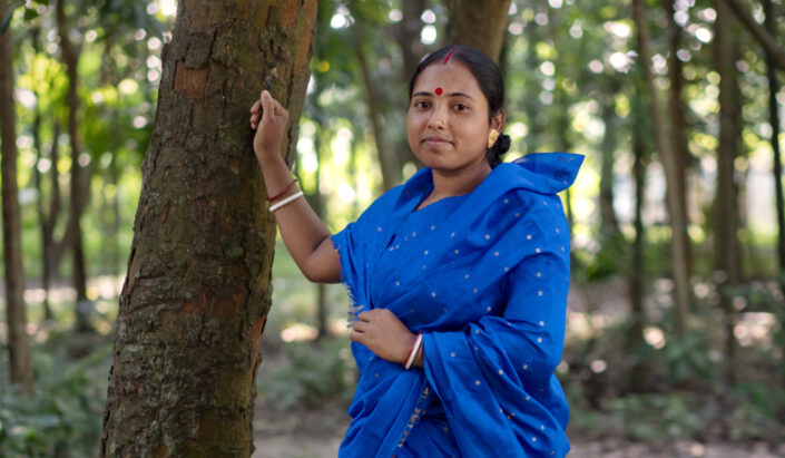 Bangladeshilainen nainen sinisessä asussa nojaa puuhun.