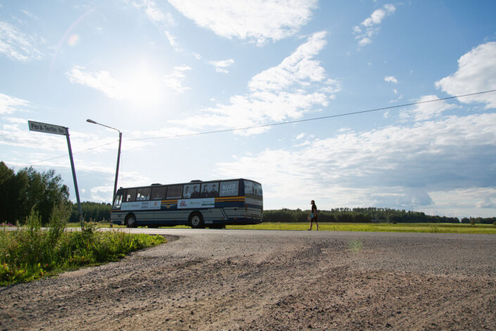 bussi on pysäköity aurinkoisena päivänä tien laitaan, sen takana mies kantaa skeittilautaa