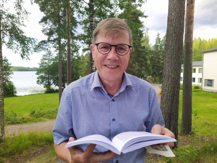 Pekka Arvio katsoo kameraan kädessään avonainen kirja.