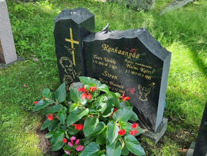 Kikan hautakivi, jossa lukee Kirsi Siren. Haudan edustalla runsaasti kukkia kesäisenvihreän ruohomaton päällä.
