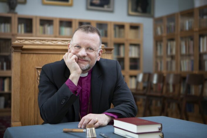 Piispa Jari Jolkkonen istumassa pöydän ääressä Raamattu edessään.