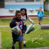 Kaksi thaimaalaista lasta juoksee muovipussit kädessä joissa on vihanneksia.