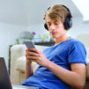 Teenage boy using smart phone while sitting in the living room during COVID-19 pandemic.