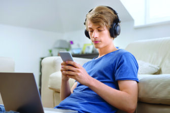 Teenage boy using smart phone while sitting in the living room during COVID-19 pandemic.