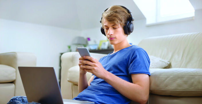 Teenage boy using smart phone while sitting in the living room during COVID-19 pandemic.