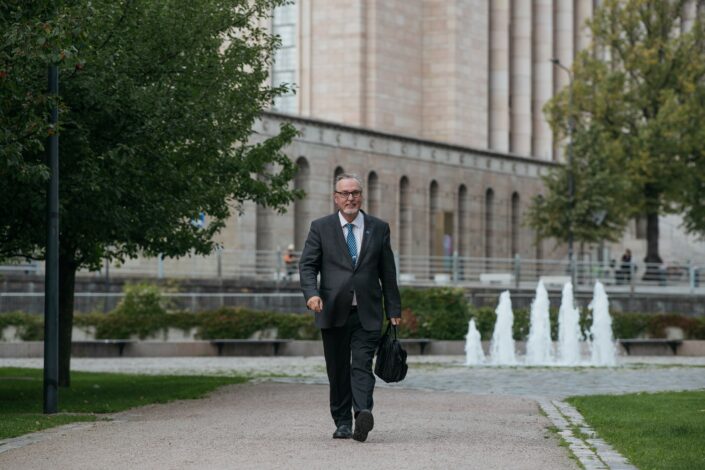 Antero Laukkanen kävelee ryhdikkäänä eduskuntatalon pilareiden edessä kadulla.