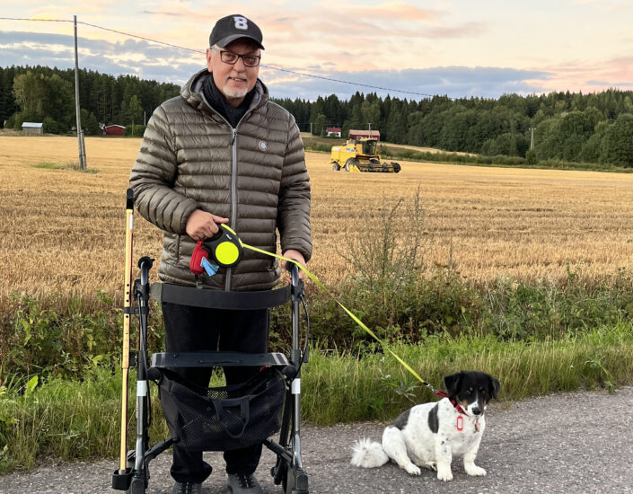 Antero Laukkanen lemmikkikoiransa kanssa pyörätuolissa keltaiseksi värjäytyneen syksyn viljavainion edessä.