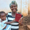 Lasta sylissään pitävä afrikkalainen äiti esittelee uutta Raamattuaan.