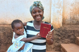 Lasta sylissään pitävä afrikkalainen äiti esittelee uutta Raamattuaan.