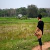 Nuori mies seisoo keskellä riisipeltoja menevällä tiellä.