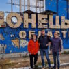 Kolme ihmistä seisoo Donetskin alueen kyltin edessä.