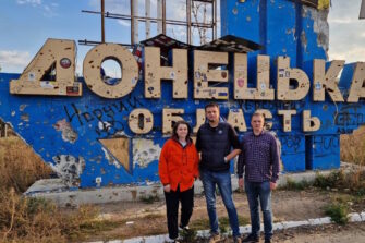 Kolme ihmistä seisoo Donetskin alueen kyltin edessä.