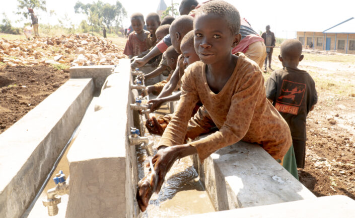 Joukko burundilaisia lapsia pesee käsiään ulkona käsienpesupaikalla.