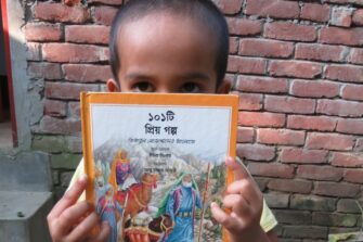 Pieni poika pitelee käsissään ja osin kasvojensa edessä lasten kristillistä kirjaa
